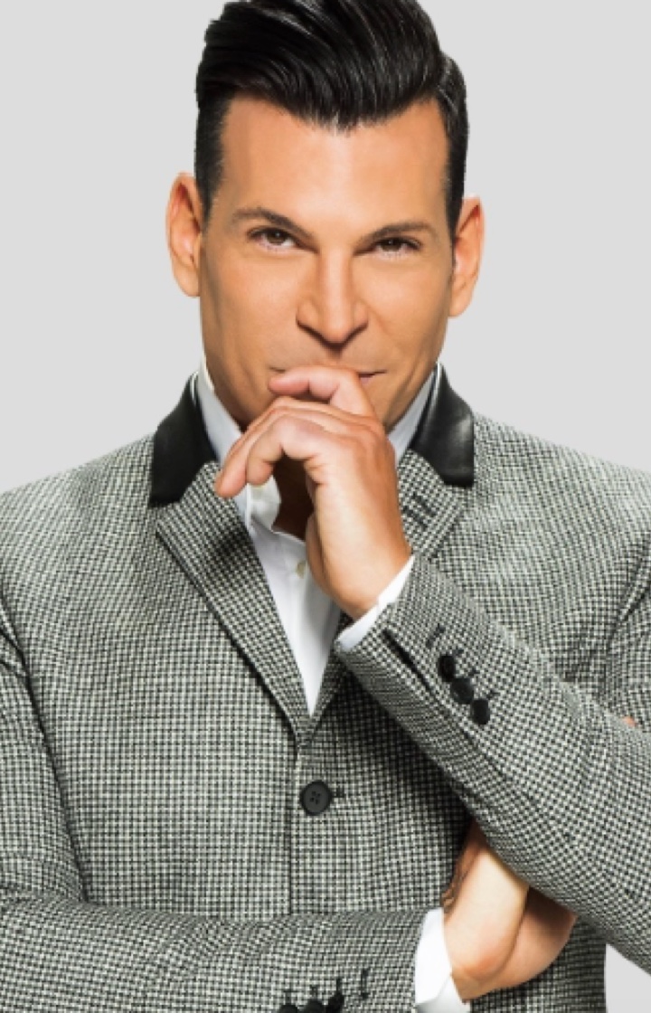 David Tutera stands in grey suit with his hand on his chin in thought.